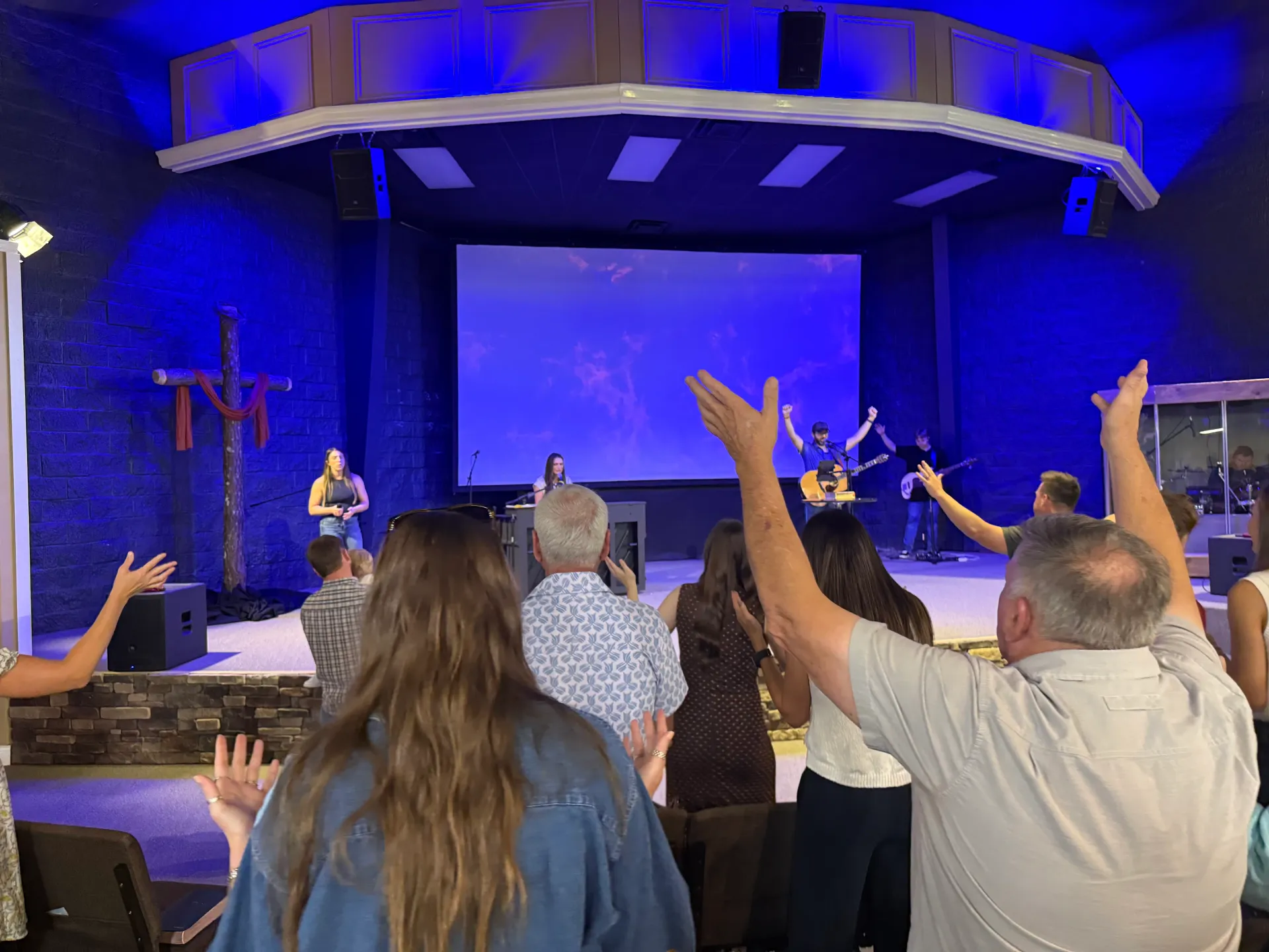 Cornerstone Assembly of God congregation worshiping with raised hands during a Sunday service.